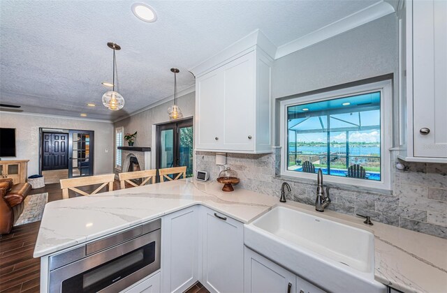 10866 Harborside Dr, Largo, FL 33773 - kitchen featuring a textured ceiling, a peninsula, open floor plan, white cabinetry, and decorative backsplash