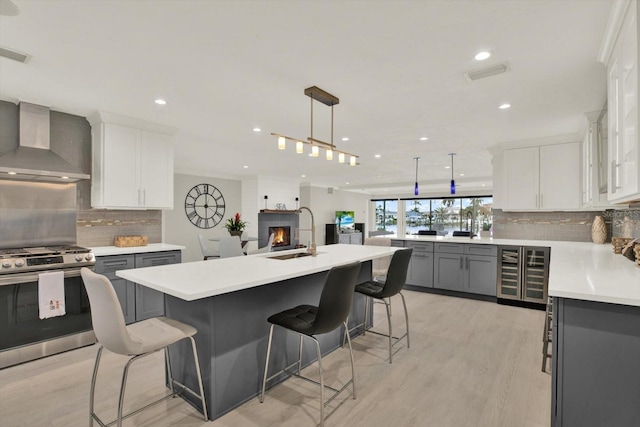 11890 Walker Ave, Seminole, FL 33772 - kitchen with wall chimney range hood, stainless steel gas stove, gray cabinetry, beverage cooler, and recessed lighting