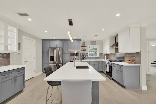 11890 Walker Ave, Seminole, FL 33772 - kitchen with stainless steel appliances, gray cabinets, wall chimney exhaust hood, decorative backsplash, and light wood-style floors
