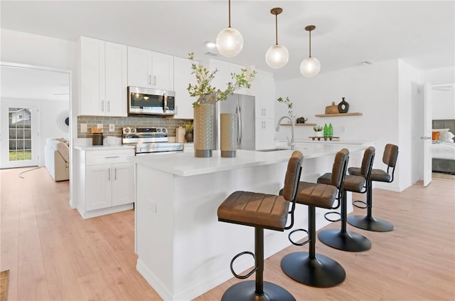 13344 Sorrento Dr, Largo, FL 33774 - kitchen with appliances with stainless steel finishes, light wood-style flooring, tasteful backsplash, a breakfast bar area, and light countertops