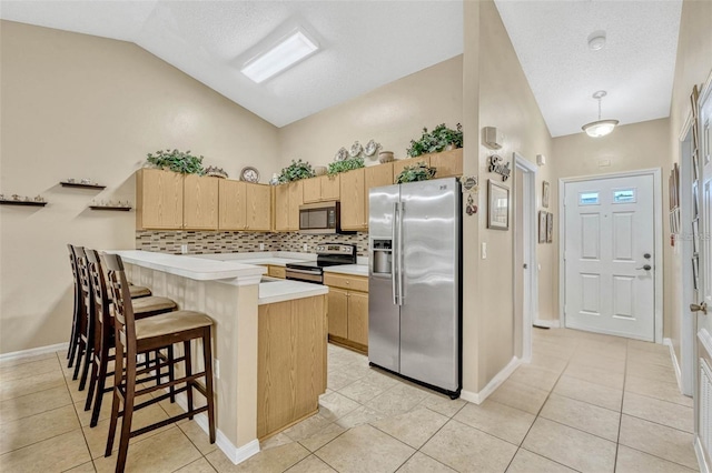 1150 Jade E Ln, Kissimmee, FL 34744 - kitchen featuring stainless steel appliances, vaulted ceiling, light brown cabinets, a peninsula, and a breakfast bar