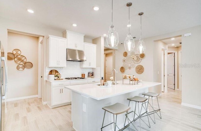 2257 Cypress Creek St, Auburndale, FL 33823 - kitchen with under cabinet range hood, appliances with stainless steel finishes, light wood-style floors, white cabinets, and a breakfast bar