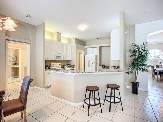 9803 Ocasta St, Riverview, FL 33569 - kitchen featuring white appliances, a peninsula, a kitchen breakfast bar, white cabinetry, and light stone counters