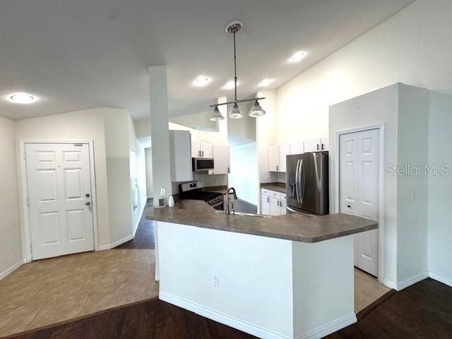 24838 Oakhaven Ct, Lutz, FL 33559 - kitchen with dark countertops, appliances with stainless steel finishes, vaulted ceiling, a peninsula, and white cabinets