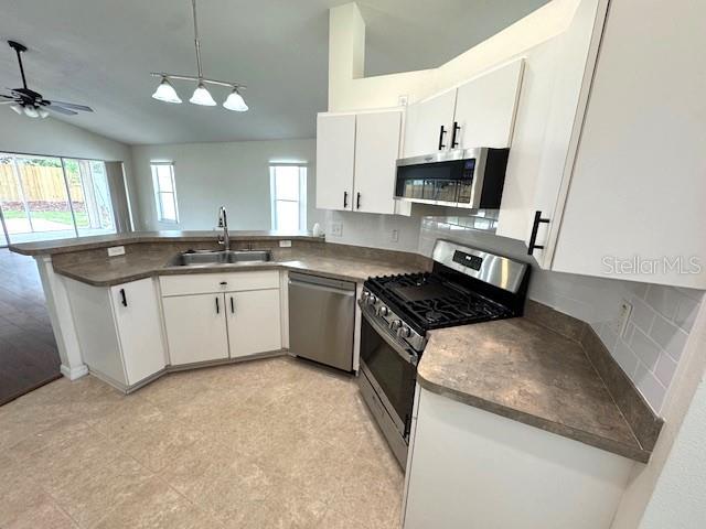 24838 Oakhaven Ct, Lutz, FL 33559 - kitchen featuring lofted ceiling, appliances with stainless steel finishes, a peninsula, white cabinetry, and tasteful backsplash