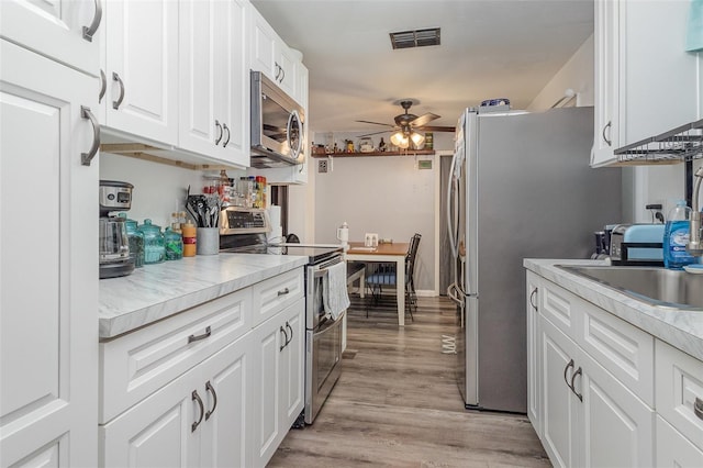 4530 David Dr, Bartow, FL 33830 - kitchen with appliances with stainless steel finishes, a ceiling fan, white cabinets, light wood-style floors, and light countertops