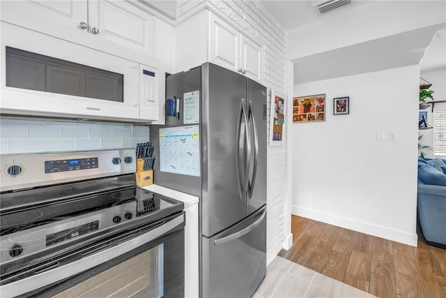 360 71st Ave, St Pete Beach, FL 33706 - kitchen featuring stainless steel electric stove, white microwave, white cabinets, light wood finished floors, and decorative backsplash