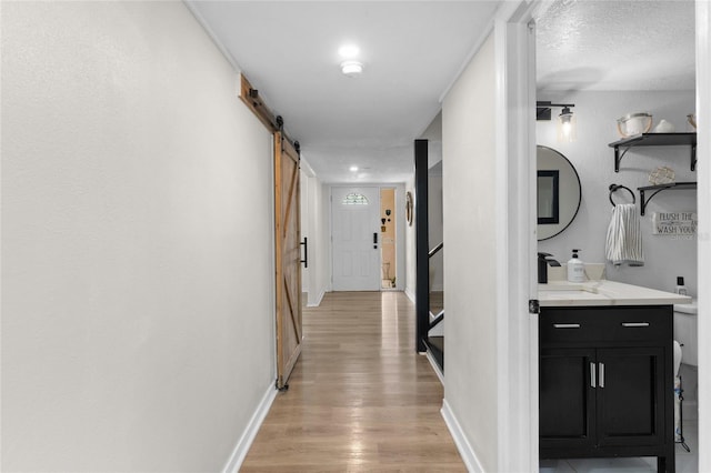 corridor featuring a barn door, light wood finished floors, and stairs