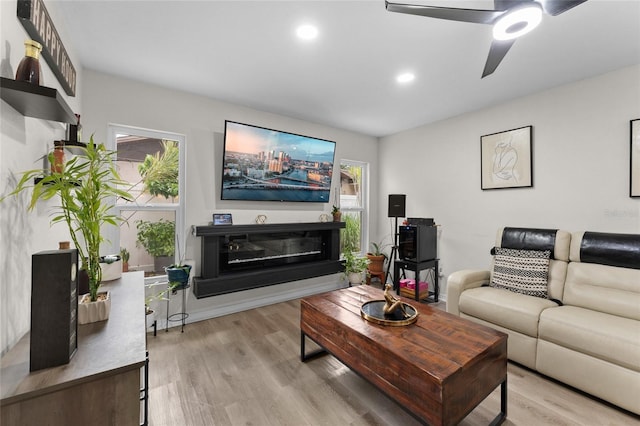 living room with a ceiling fan, light wood-style floors, recessed lighting, and a glass covered fireplace