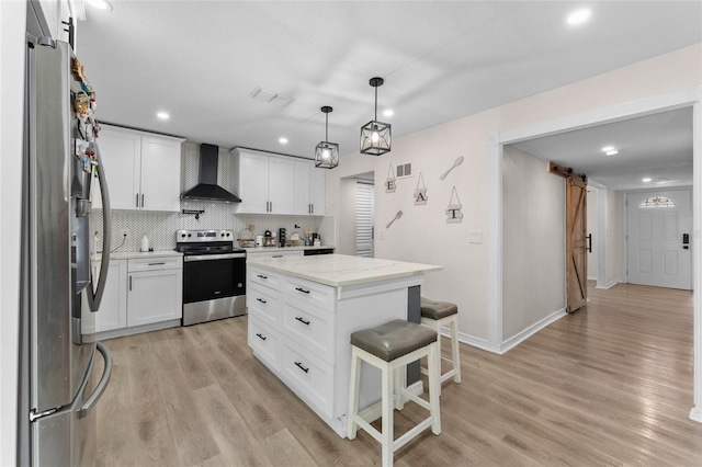 kitchen featuring a barn door, stainless steel appliances, wall chimney exhaust hood, light wood-style flooring, and recessed lighting