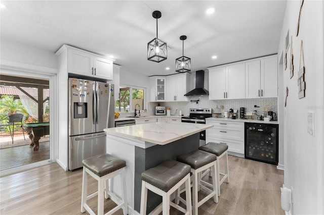 kitchen with stainless steel appliances, wine cooler, light wood-style flooring, wall chimney range hood, and recessed lighting