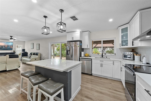 kitchen with appliances with stainless steel finishes, decorative backsplash, white cabinets, a kitchen island, and recessed lighting