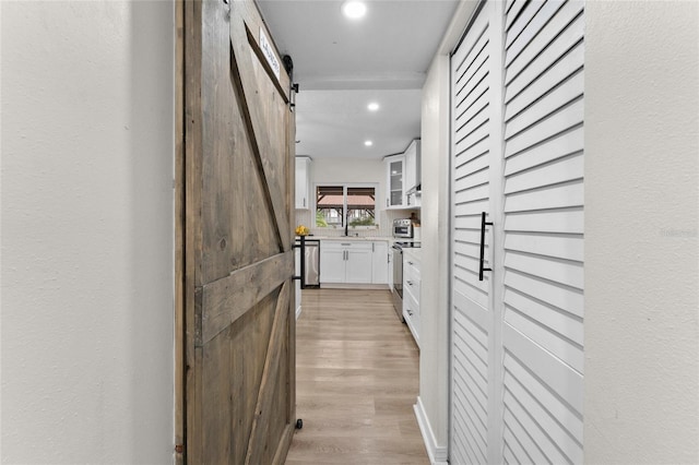 hall featuring a barn door, light wood finished floors, and recessed lighting