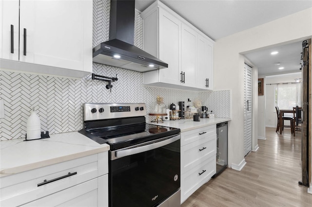 kitchen featuring stainless steel range with electric stovetop, wall chimney range hood, decorative backsplash, and white cabinets
