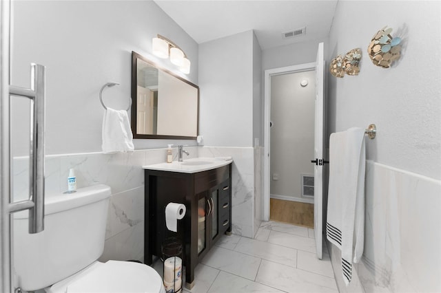 bathroom featuring marble look tiles, vanity, wainscoting, and tile walls