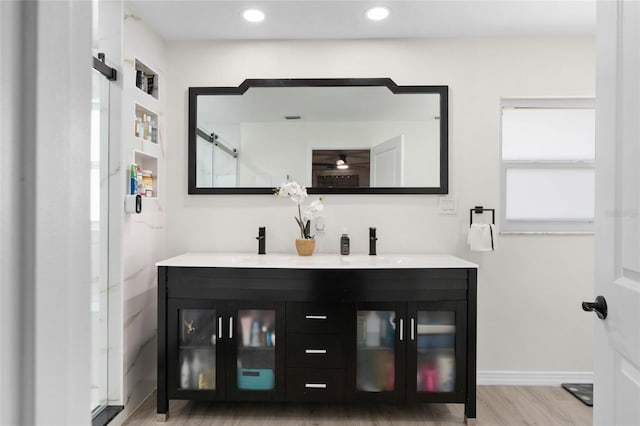 bathroom with double vanity, a marble finish shower, wood finished floors, and recessed lighting