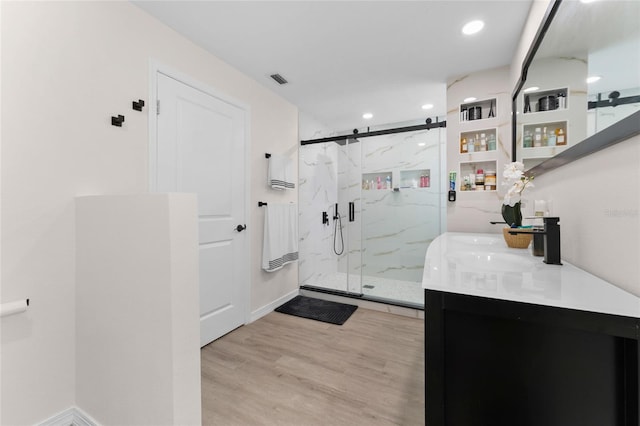 bathroom featuring a marble finish shower, wood finished floors, vanity, and recessed lighting