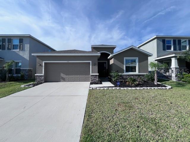 144 Bright Ibis Ave, Apollo Beach, FL 33572 - view of front of house with stone siding, an attached garage, concrete driveway, and stucco siding