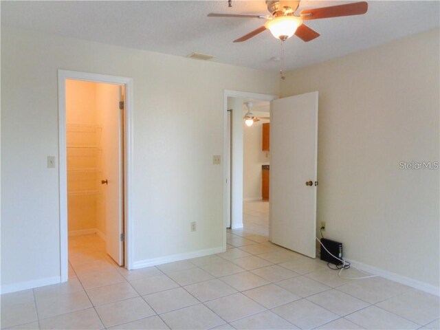 unfurnished bedroom featuring a spacious closet, a closet, ceiling fan, and light tile floors