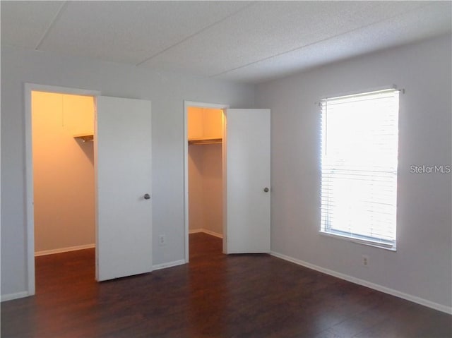 unfurnished bedroom featuring dark wood-type flooring, a walk in closet, and a closet