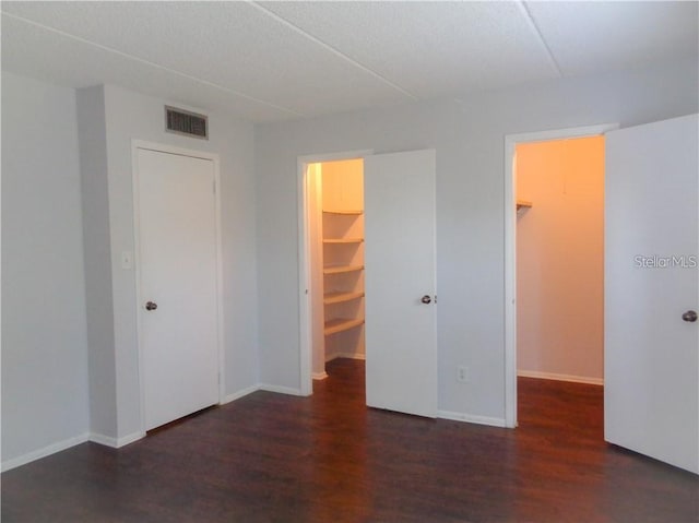 unfurnished bedroom with a walk in closet, dark hardwood / wood-style flooring, and a closet