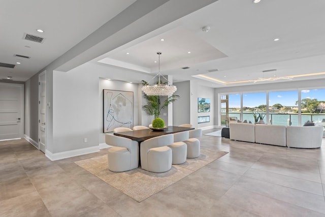 dining space with a tray ceiling, a water view, and an inviting chandelier