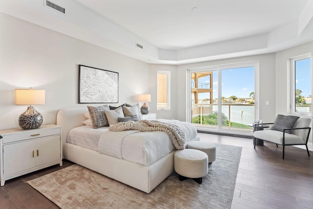 bedroom featuring a raised ceiling, a water view, and dark hardwood / wood-style floors