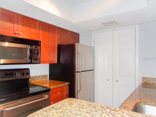 kitchen with stainless steel appliances, a textured ceiling, and light stone counters