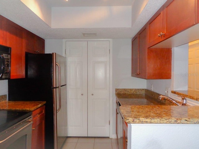 kitchen with a tray ceiling, light stone countertops, light tile floors, and range