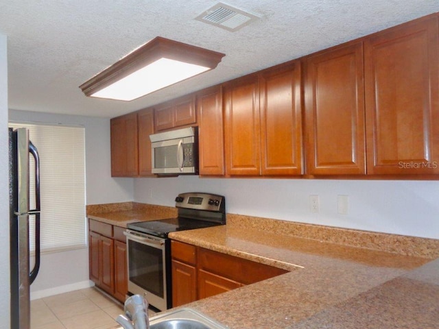 kitchen with light tile floors, a textured ceiling, light stone counters, and stainless steel appliances