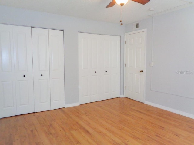 unfurnished bedroom featuring multiple closets, light hardwood / wood-style floors, and ceiling fan