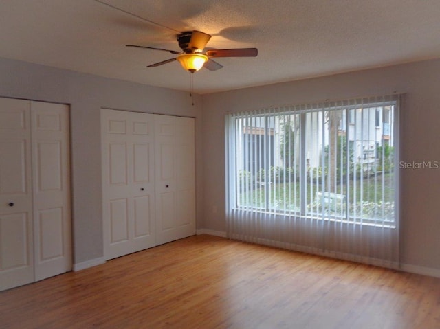 unfurnished bedroom featuring multiple windows, two closets, ceiling fan, and light wood-type flooring