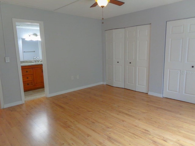 unfurnished bedroom featuring ensuite bath, ceiling fan, light hardwood / wood-style floors, and two closets