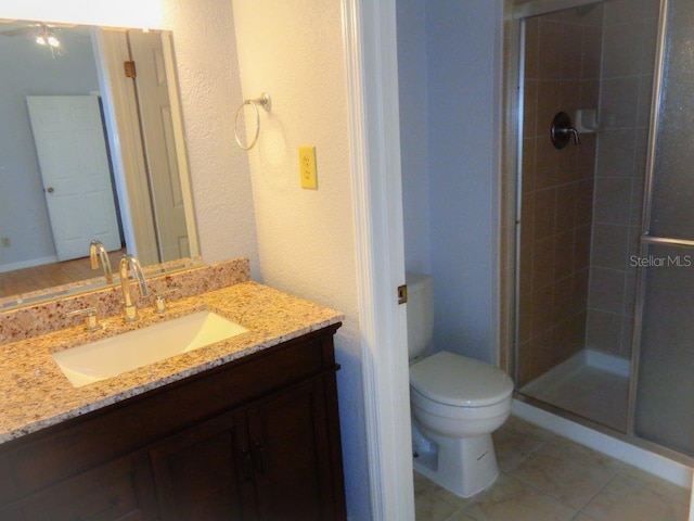 bathroom with toilet, vanity, a shower with shower door, and tile flooring