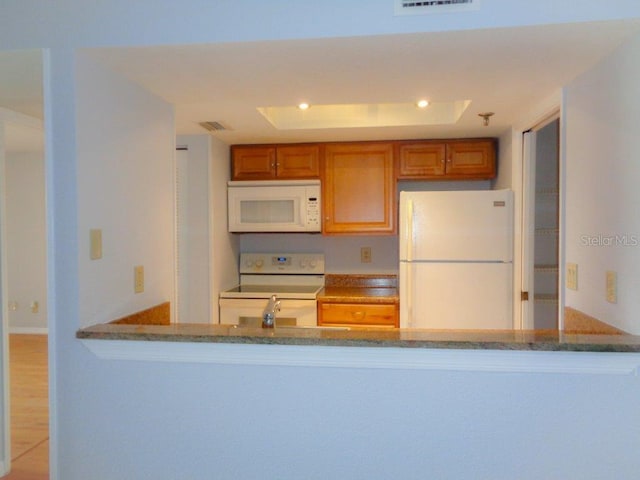 kitchen with white appliances, sink, dark stone counters, a tray ceiling, and light wood-type flooring