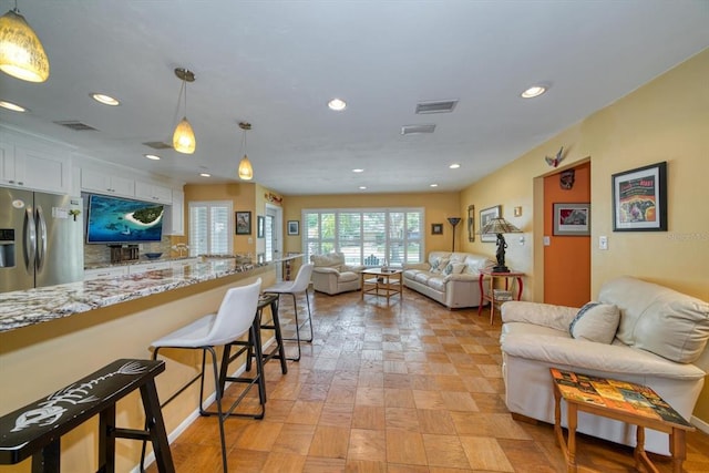 kitchen with stainless steel fridge with ice dispenser, a kitchen breakfast bar, hanging light fixtures, and white cabinetry