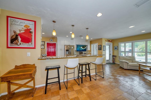 kitchen with kitchen peninsula, light stone counters, stainless steel fridge with ice dispenser, white cabinets, and decorative light fixtures