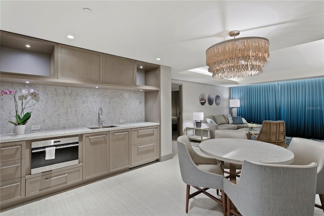 kitchen featuring a notable chandelier, stainless steel oven, sink, hanging light fixtures, and light stone counters