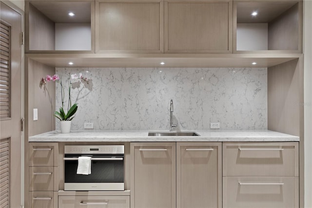 kitchen featuring wall oven, tasteful backsplash, light stone counters, and sink