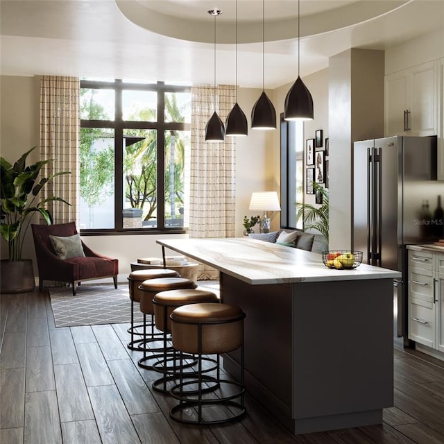 kitchen with a tray ceiling, dark wood-type flooring, a kitchen bar, a kitchen island, and pendant lighting