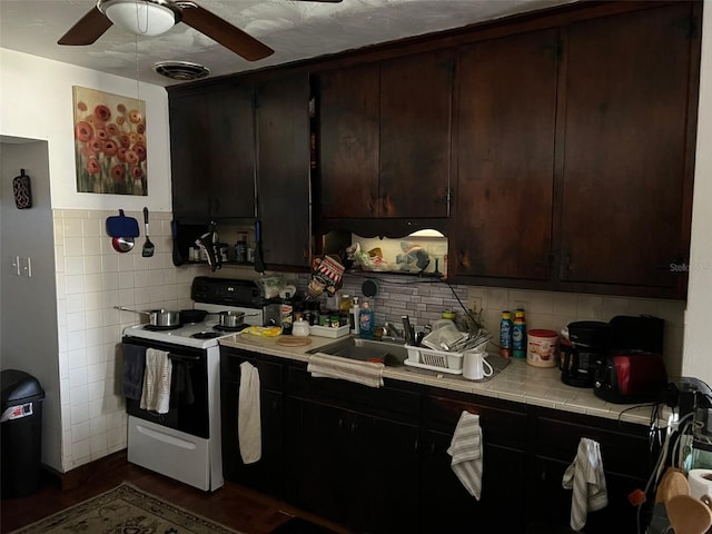 kitchen featuring sink, ceiling fan, electric range, dark brown cabinets, and tile counters