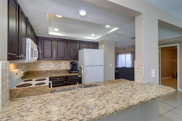 kitchen with white appliances, sink, dark brown cabinets, backsplash, and a tray ceiling