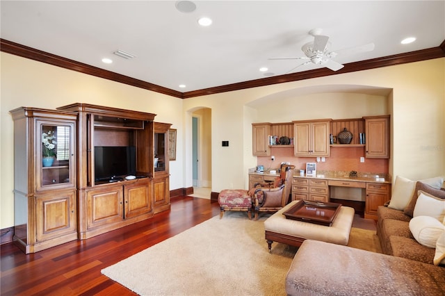 living room with ornamental molding, built in desk, ceiling fan, and dark wood-type flooring