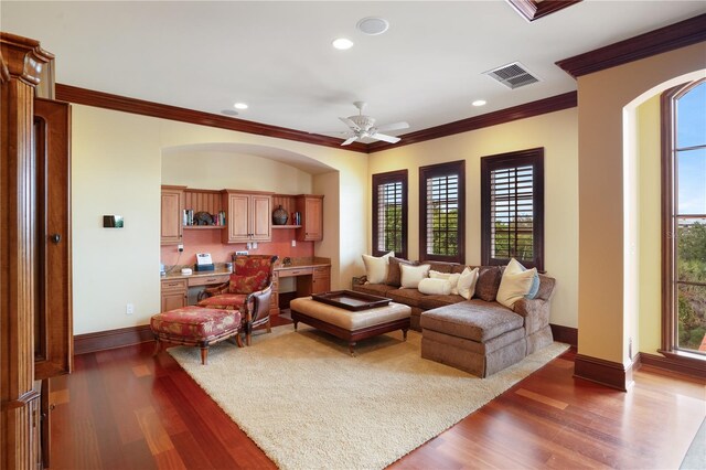 living room with built in desk, crown molding, ceiling fan, and dark wood-type flooring