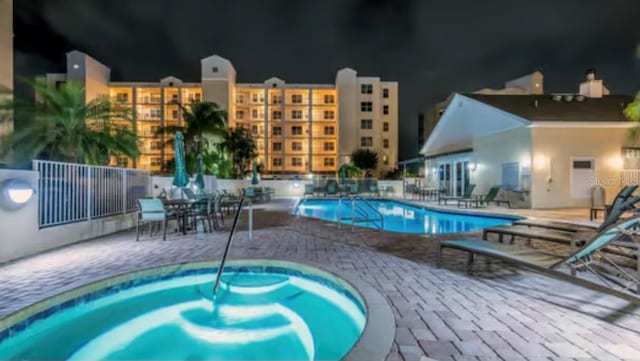 pool at twilight with a community hot tub and a patio area