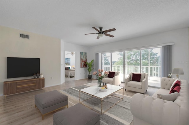 living room with a textured ceiling, ceiling fan, and light hardwood / wood-style flooring