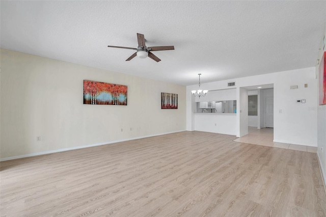 unfurnished living room with a textured ceiling, ceiling fan with notable chandelier, and light tile floors