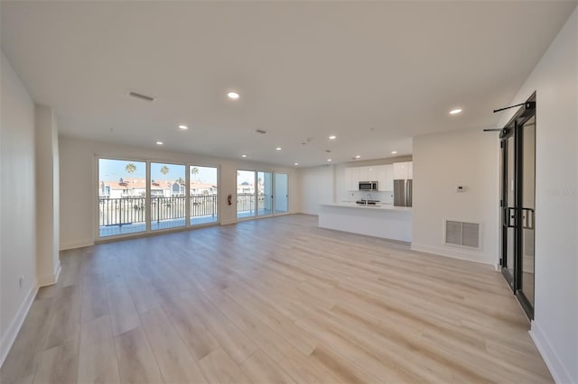 unfurnished living room with light wood-type flooring, a barn door, visible vents, and recessed lighting