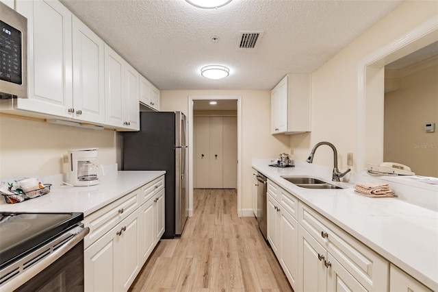 kitchen with light wood finished floors, visible vents, appliances with stainless steel finishes, white cabinets, and a sink