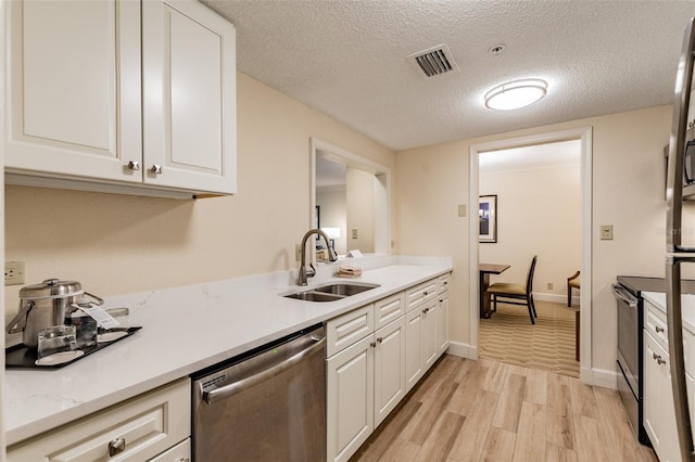 kitchen with visible vents, stainless steel appliances, light wood-type flooring, white cabinetry, and a sink